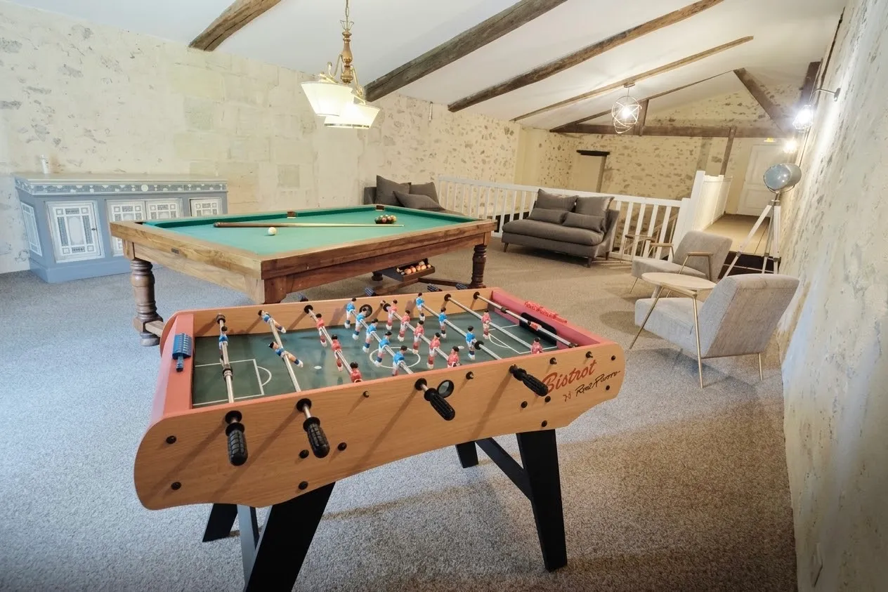 Salle de jeux du Château Meyre avec baby-foot, billard et fauteuils sous des poutres apparentes.