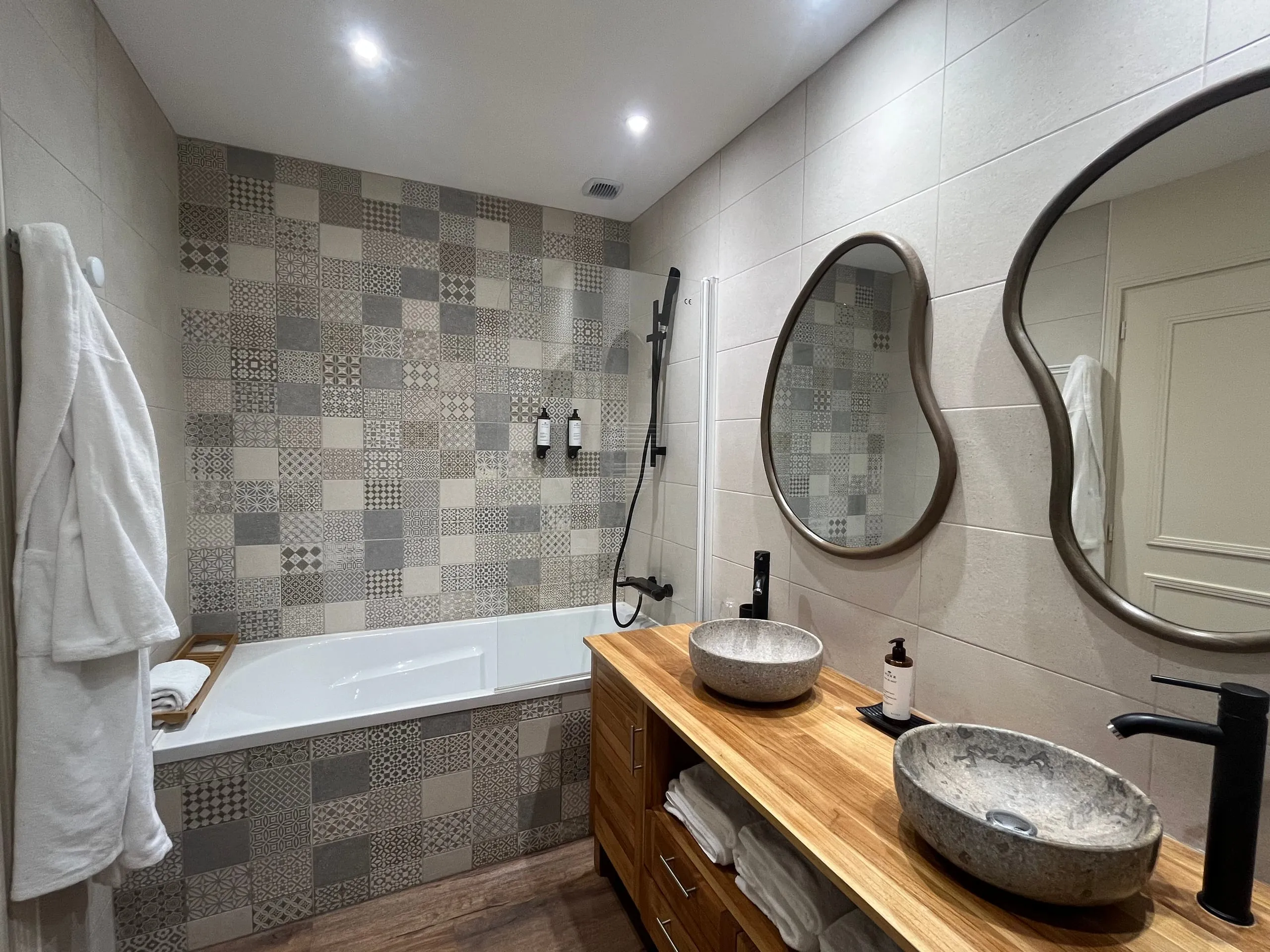 Salle de bain de la chambre Cybele avec baignoire, deux vasques en pierre et carrelage à motifs.