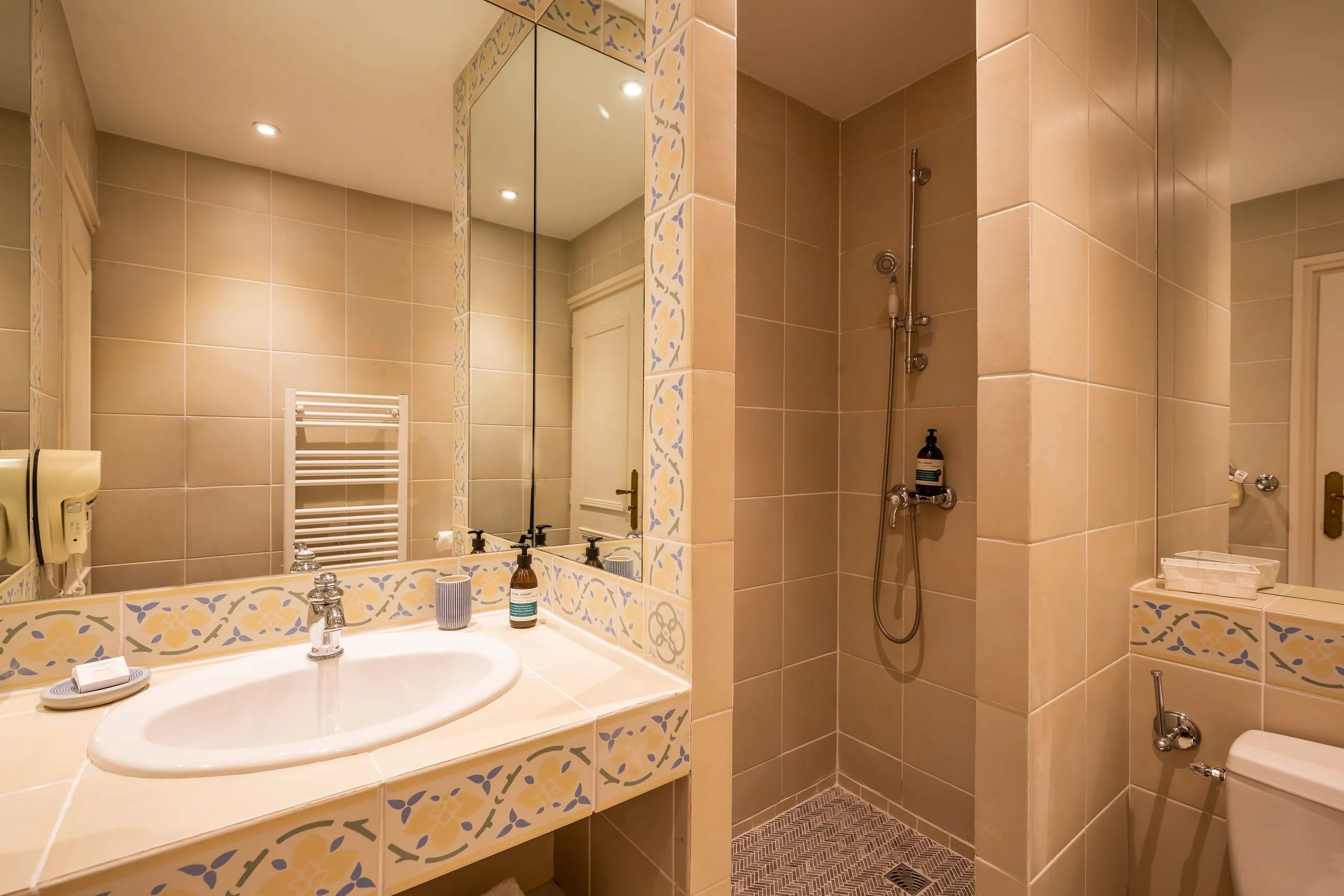 Salle de bain de la chambre Luna avec douche, lavabo et carrelage décoratif beige et bleu.