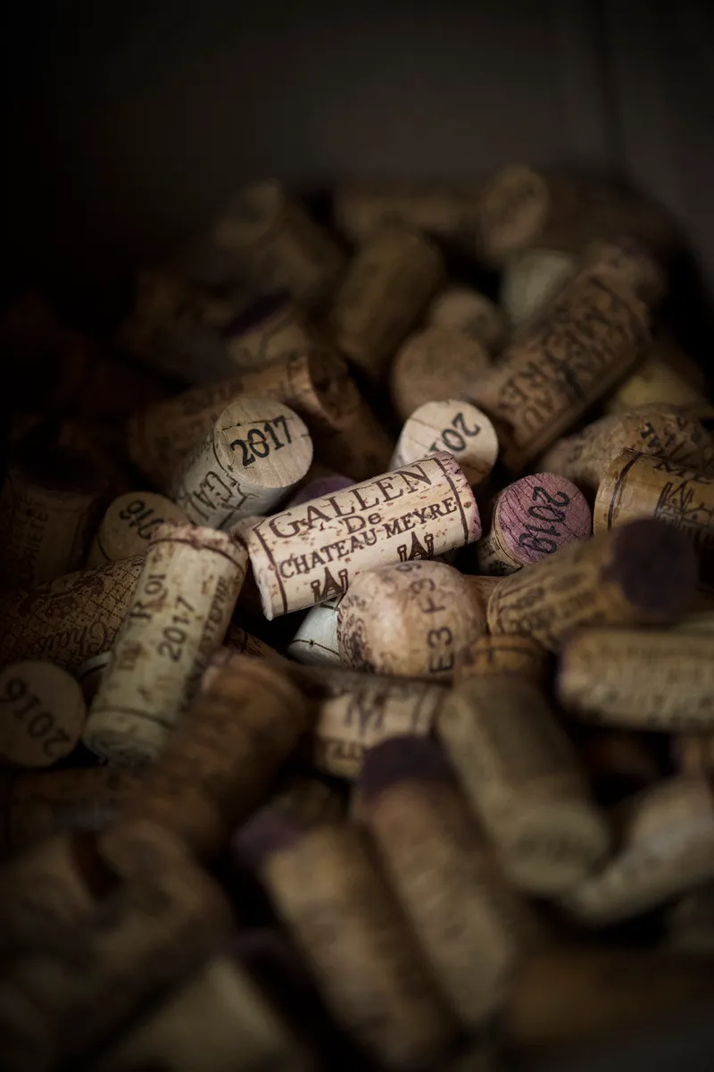 Bouchons marqués Château Meyre posés devant des bouteilles de vin.