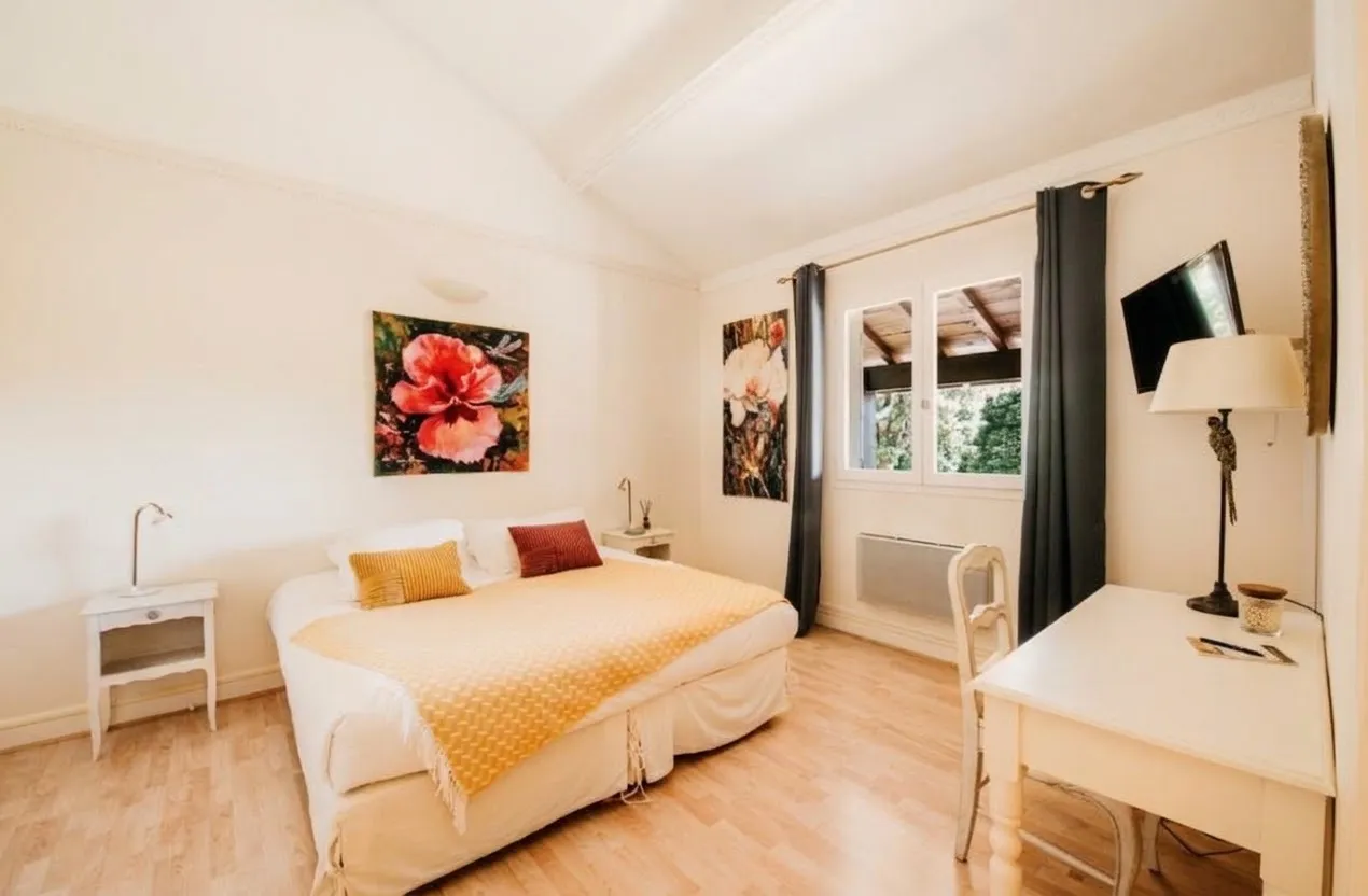 Chambre Ceres lumineuse avec grand lit, bureau blanc et tableaux floraux.