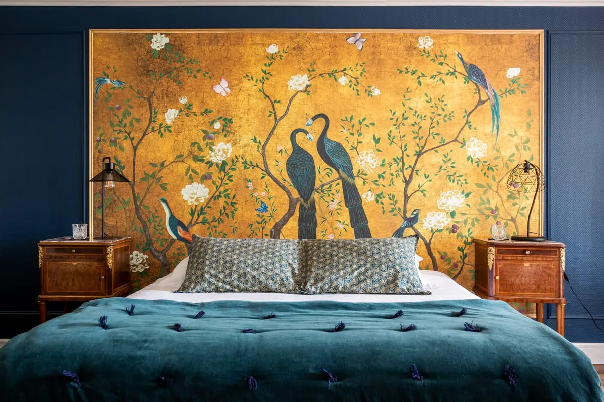 Lit double de la chambre Maïa devant un panneau doré décoré d'oiseaux et de fleurs au Clos de Meyre.