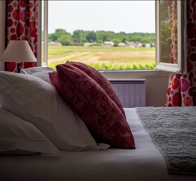Lit d’une chambre du Clos de Meyre avec fenêtre ouverte sur le vignoble à Avensan.