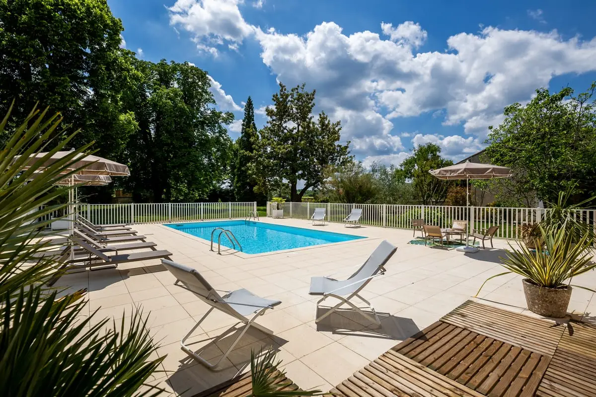 Piscine extérieure du Clos de Meyre entourée de transats et d’un parc arboré.